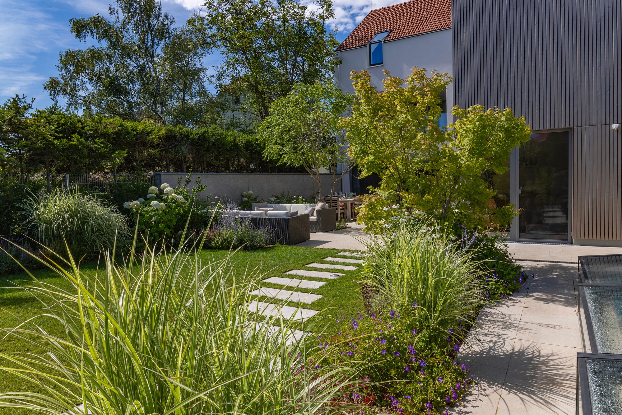 Modern gestalteter Garten mit Rasenfläche, Staudenbeeten und Sitzbereich auf der Terrasse