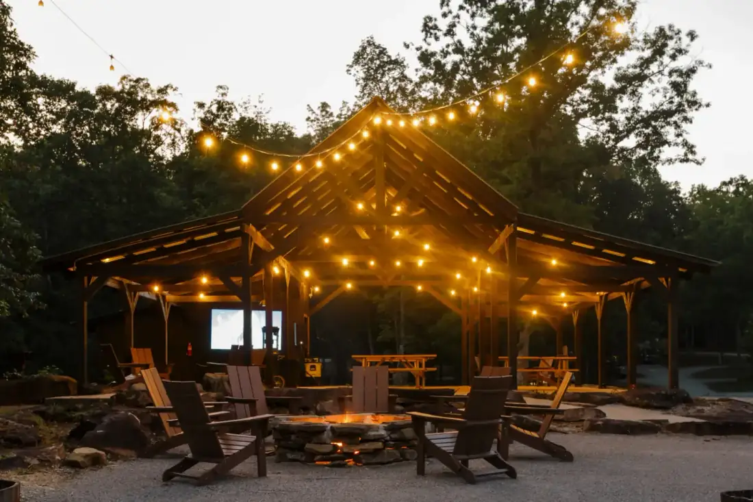 Campers gathered around the fire pit under string lights at night