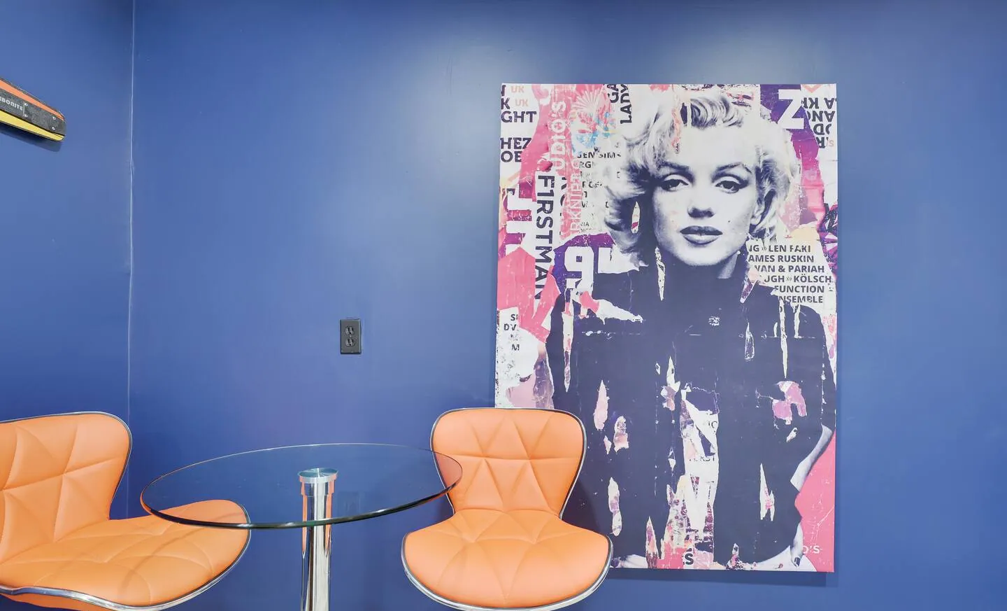 Game corner with orange bar stools and pop art portrait on blue wall at The Love Shack