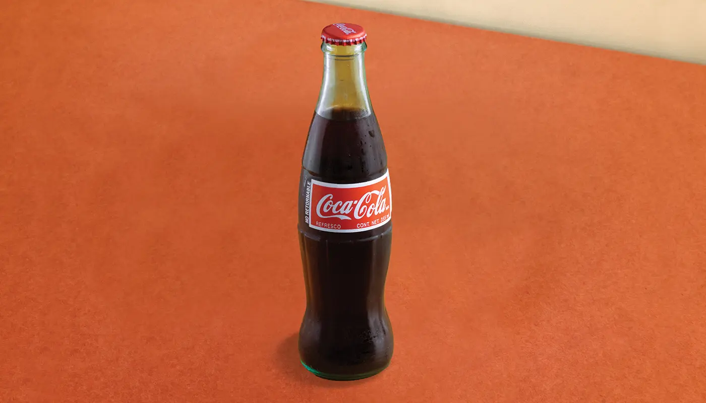A glass Coca-Cola bottle filled with dark soda and capped with a red metal cap.
