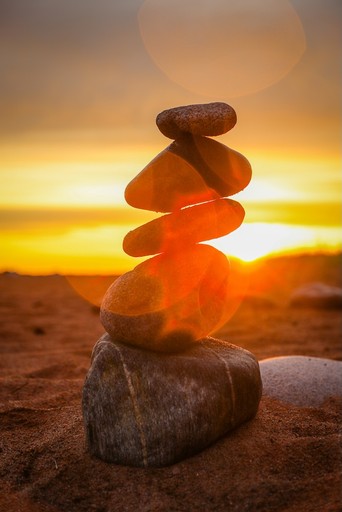 Steinnmännchen an einem Strand im Sonnenuntergang, symbolisiert Gleichgewicht und Balance.