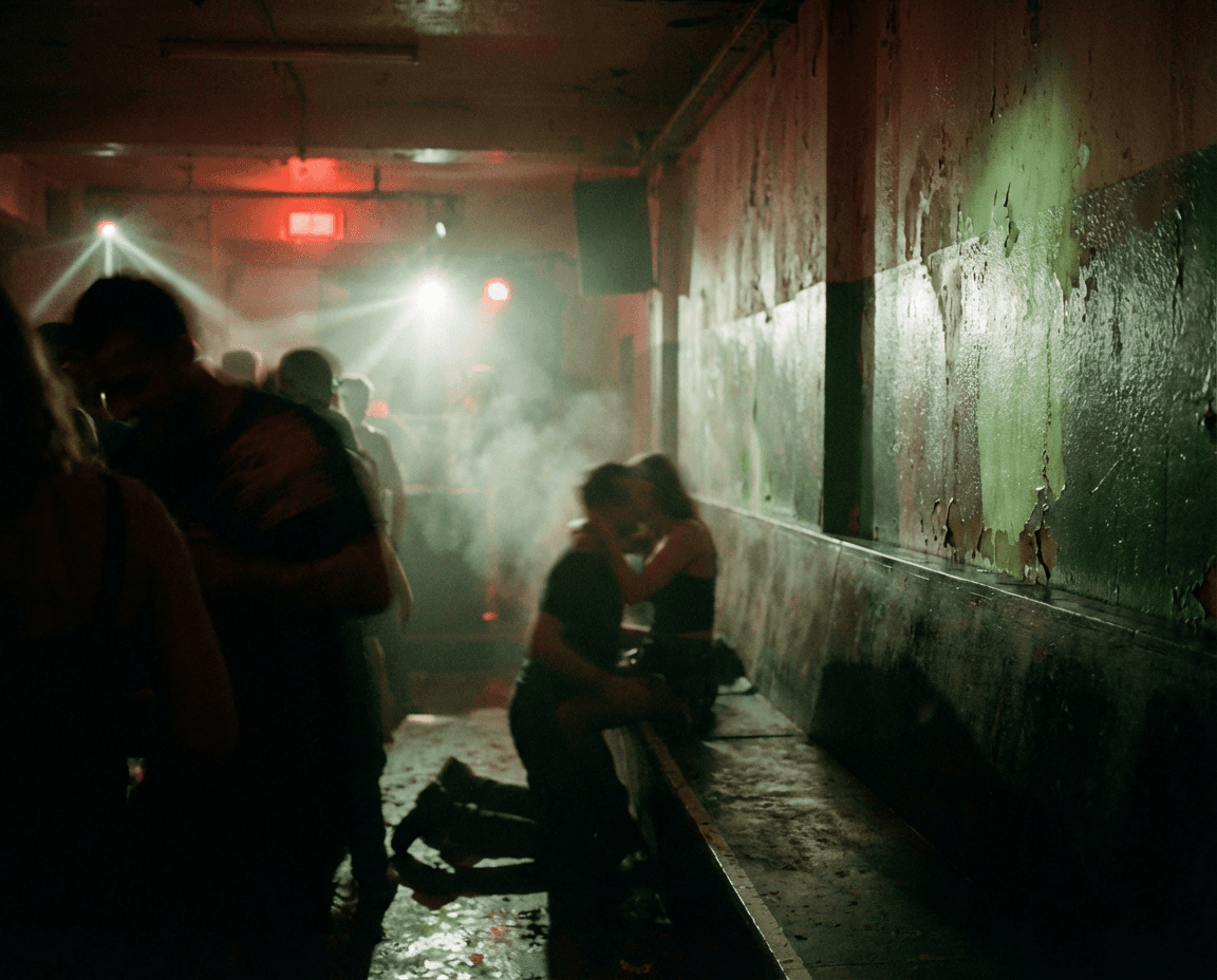 A dimly lit, underground nightclub scene where couples embrace on worn benches and dancers move through hazy light beams, capturing the raw intimacy, atmosphere, and grit of late-night Berlin club culture.