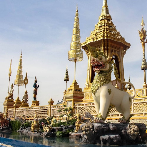 一个装饰华丽的泰国寺庙，点缀着金色尖顶、精致的雕像，以及庙前的一个大型神兽雕塑。