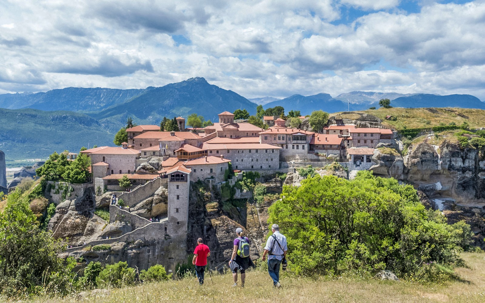 Gasten wandelen naar het Meteora-klooster met de bergen op de achtergrond.