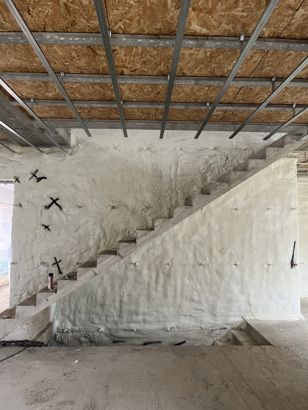 Technicien portant une combinaison de protection appliquant de la mousse de polyuréthane sur un mur dans un bâtiment en construction.