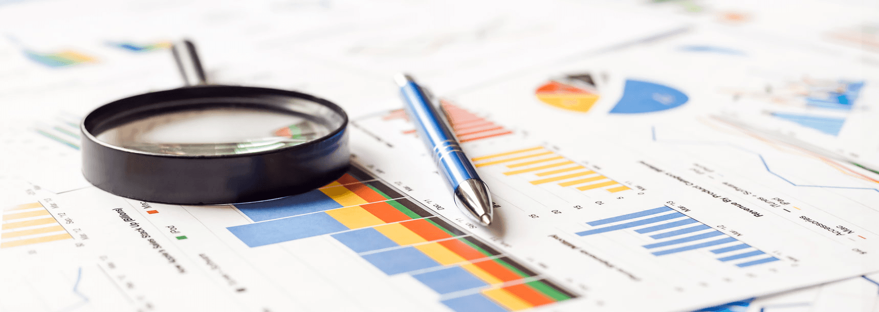 Magnifying glass and pen on charts - How to Calculate Total Revenue in Excel