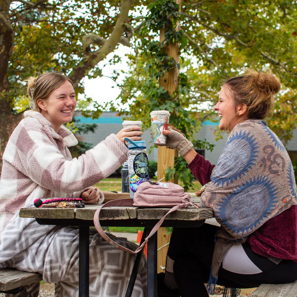 A photo of two girls sitting at a picnic table enjoying RoosRoast coffee