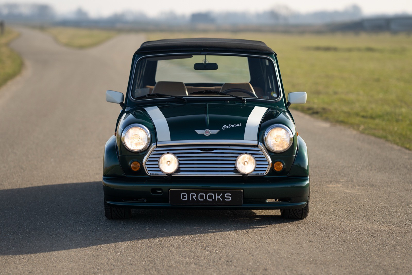 A classic black car with chrome details parked on a paved road, surrounded by open fields under a clear sky.
