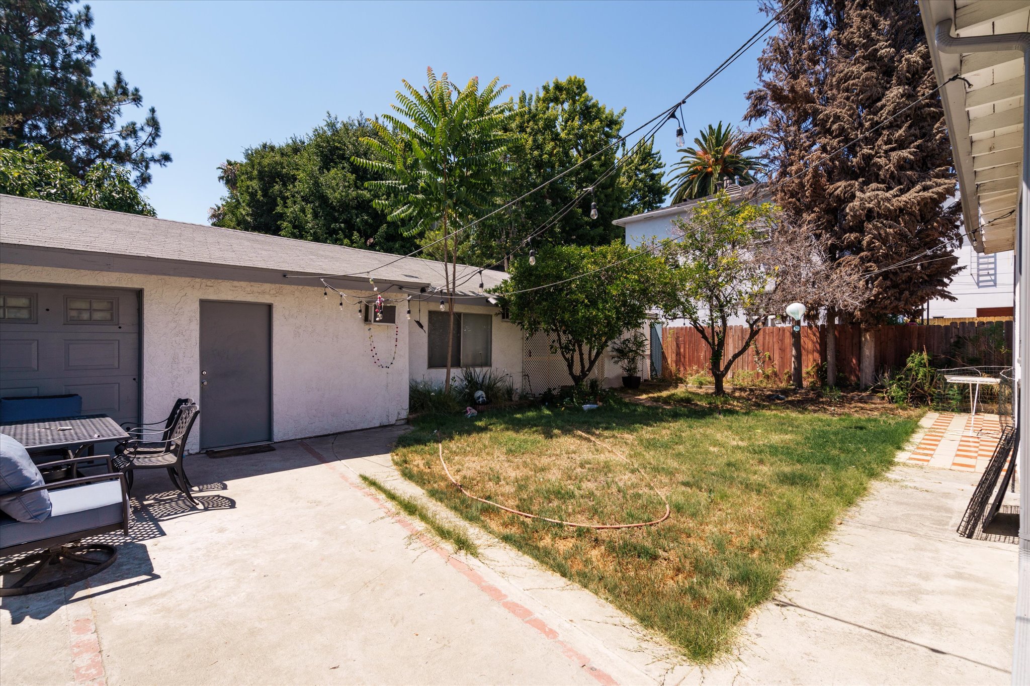 A sunny backyard scene at 1807 n van ness, featuring a small lawn, trees, a garage, and a paved pathway.