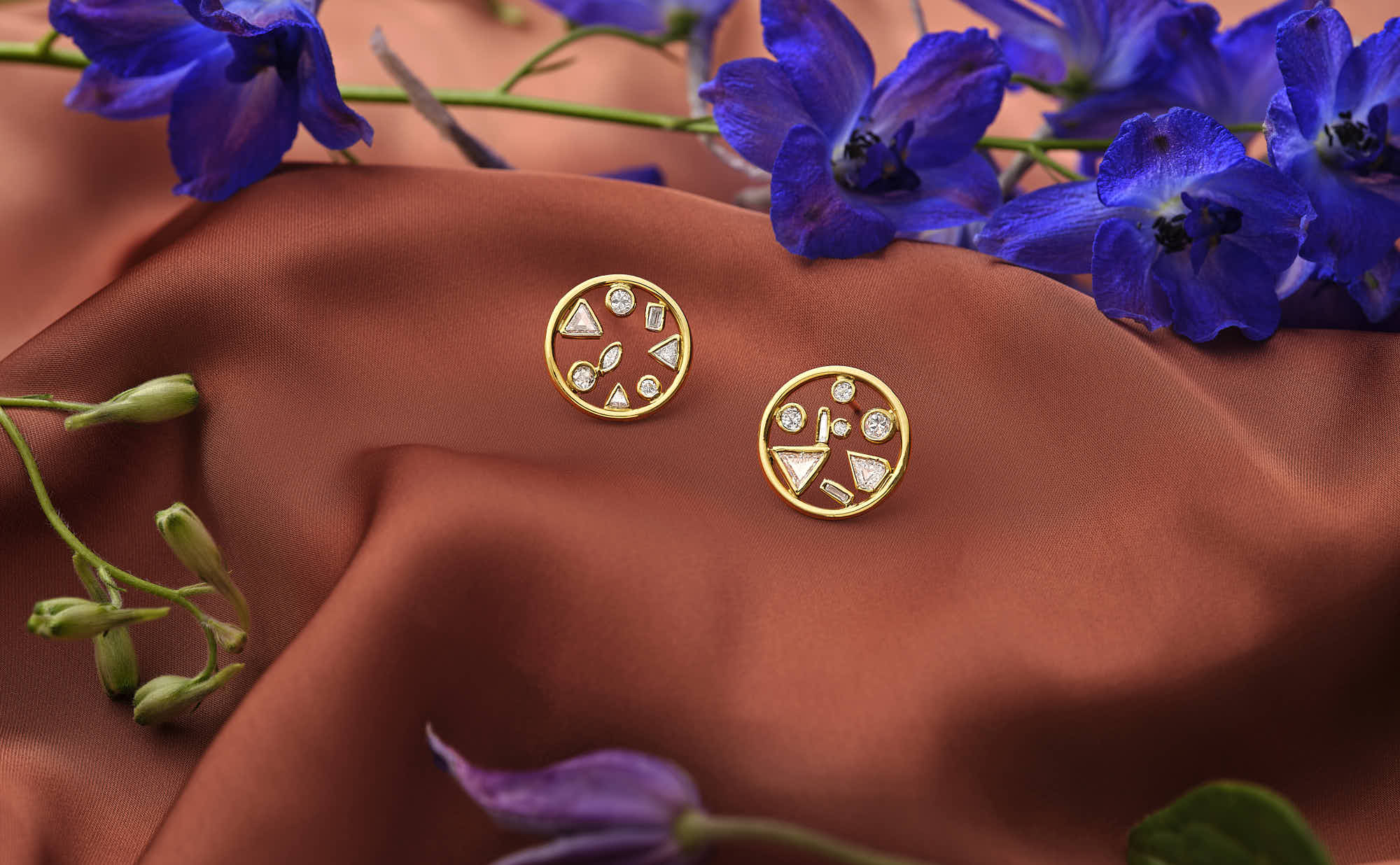 Gold geometric stud earrings on silky red fabric with purple flowers.
