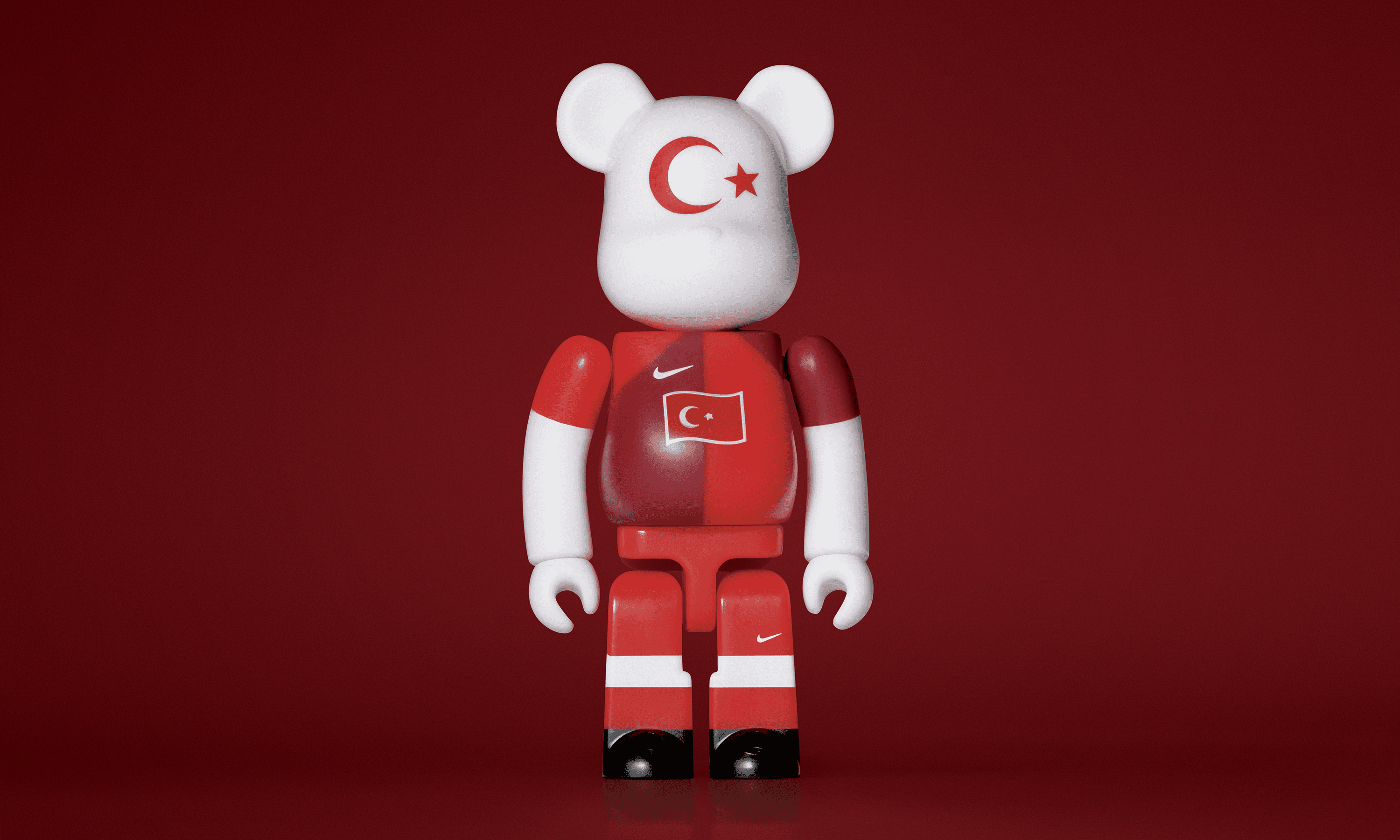 A single 3.5” tall Bre@rbrick/Nike toy created to commemorate the 2006 Turkish World Cup football team. The toy is painted to appear in the Turkish football kit and stands in the center of the frame in front of a dark red background. 