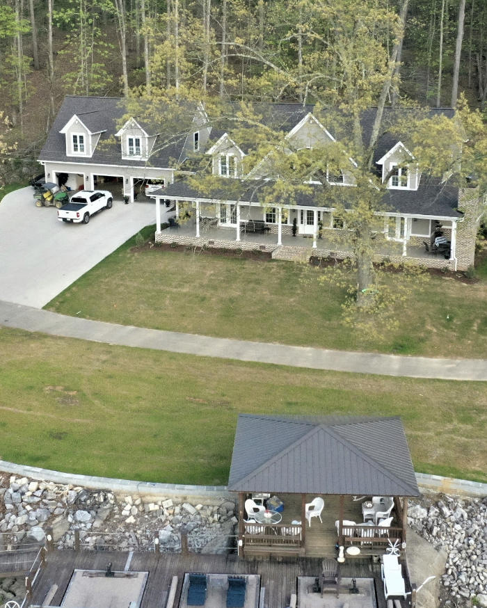 Aerial view of a spacious home with a manicured lawn and a patio area in a wooded setting.