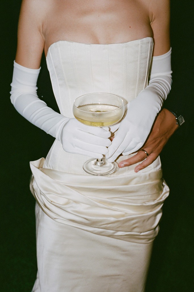 Bride holding a coupe glass in a corseted wedding dress with long white gloves