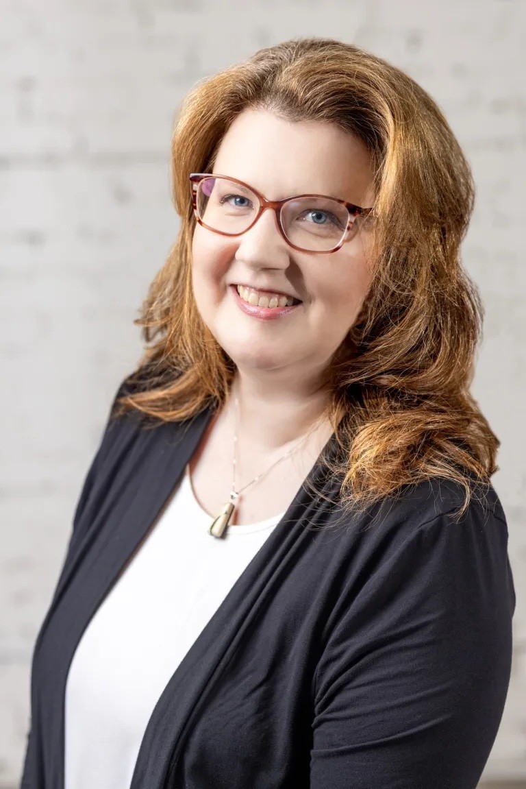 Image of Woman with glasses smiling in front of a neutral background with a professional demeanor in interior design.