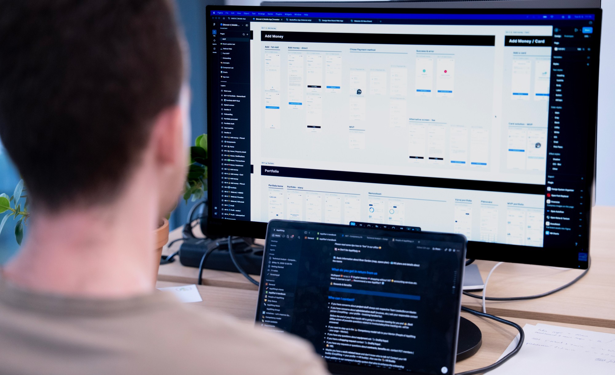 A product manager at a desk reviews app design mockups on a monitor, with notes open on a laptop beside them