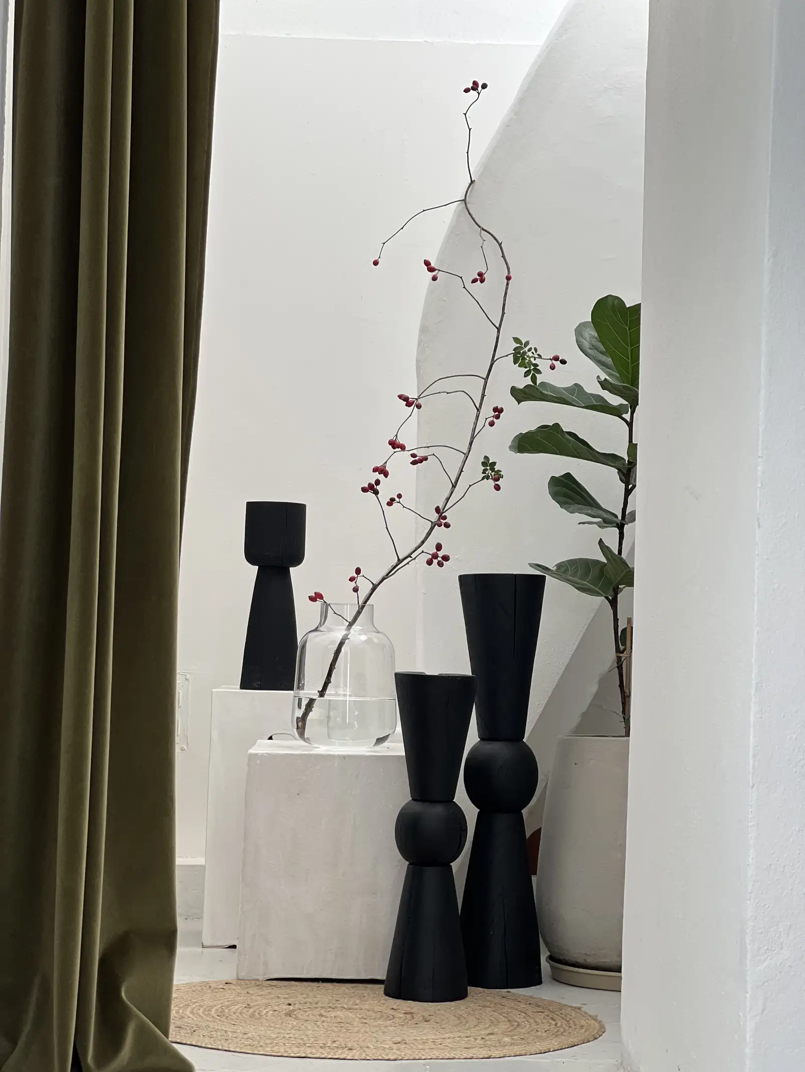 Escena interior con esculturas negras y rama roja en florero transparente para fotógrafos de espacios que buscan equilibrio entre forma y vacío