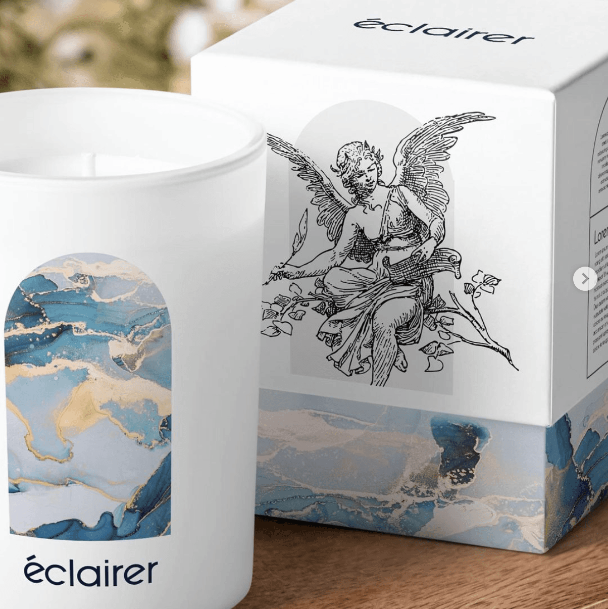 A decorative candle in a white container beside its artistic box featuring an intricate design.