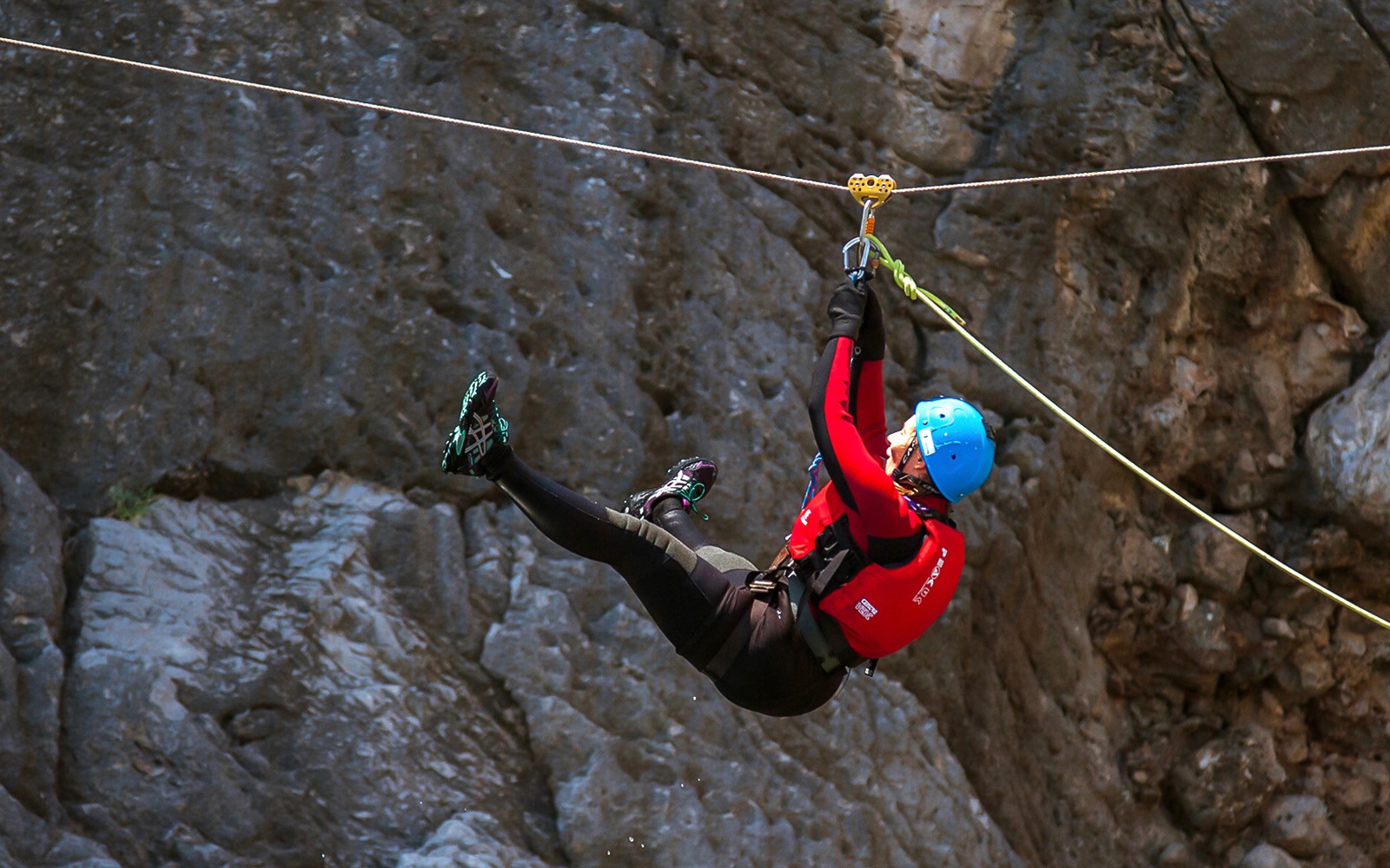Coasteering-deltaker i zipline over steinete terreng.