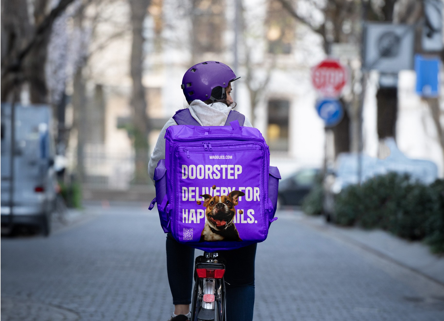 A rear medium shot of a cyclist riding her bike whilst wearing a purple back pack