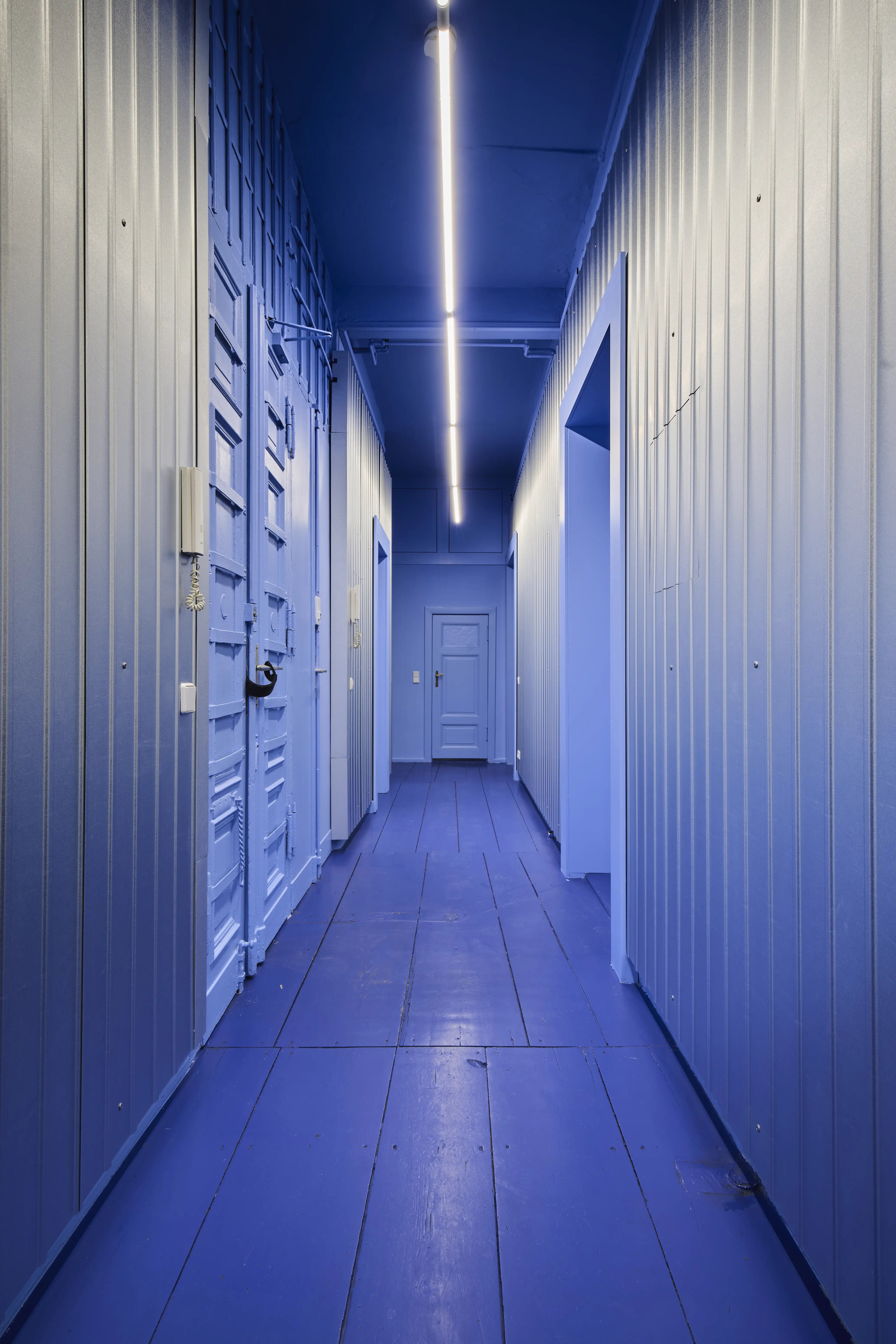 Monochrome periwinkle blue hallway with panelled walls, doors and LED light line on the ceiling.