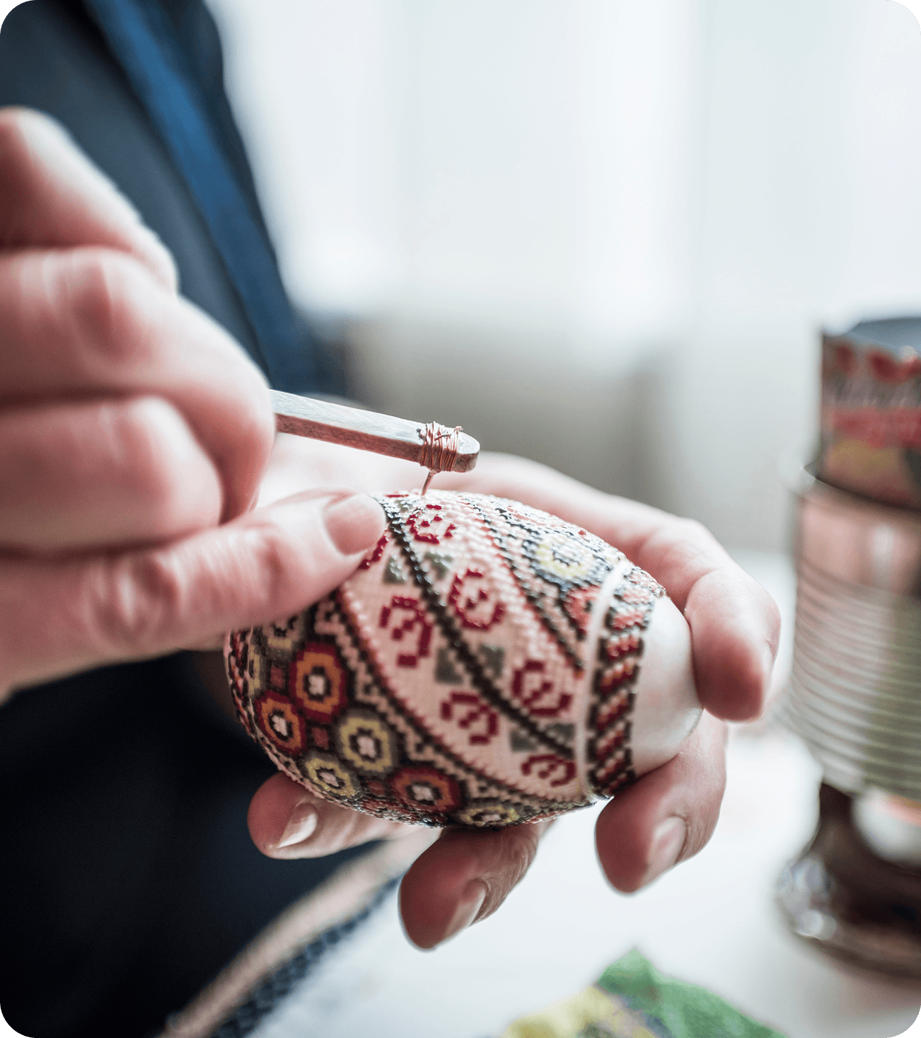 Hands decorating a Ukrainian Pysanka Easter egg with wax resist technique.