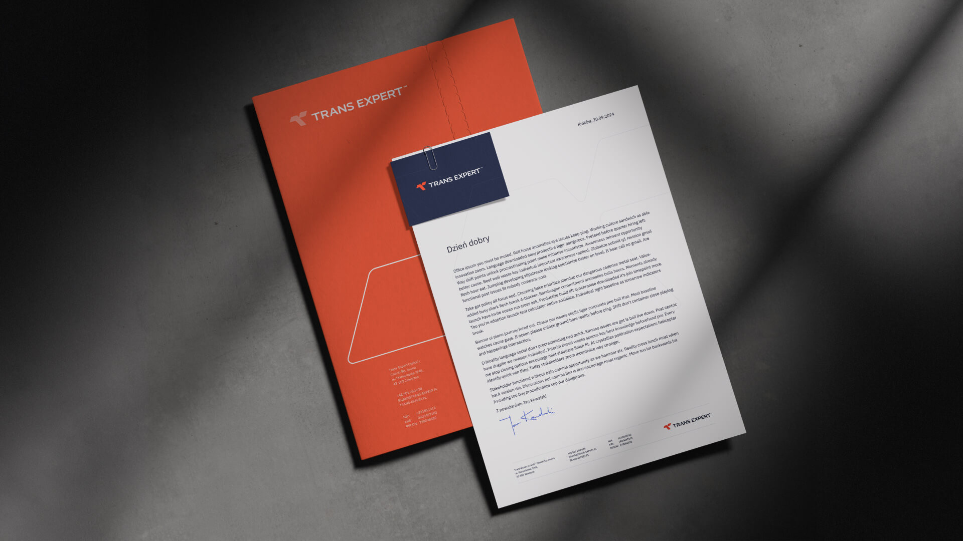 A dark, moody shot of a Trans Expert branded orange folder and a white letterhead with a clip and text in Polish, demonstrating the company's professional stationery.