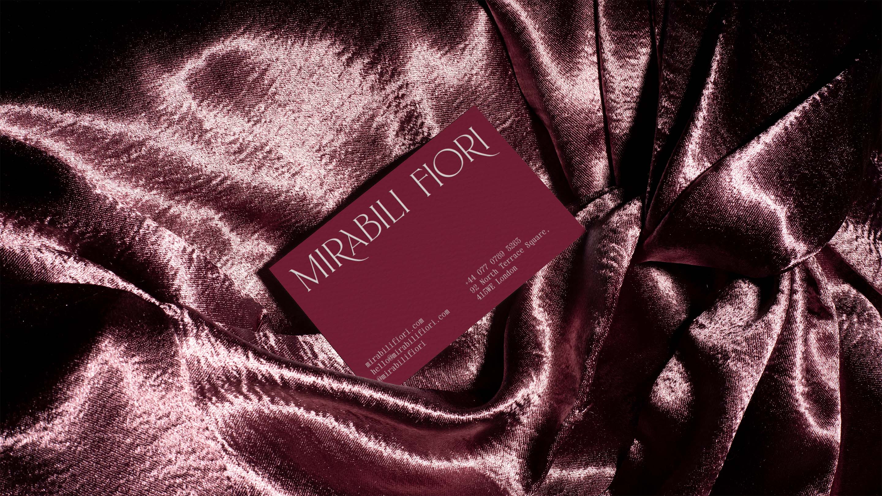 Burgundy business card on shimmering velvet fabric showing contact details in white text
