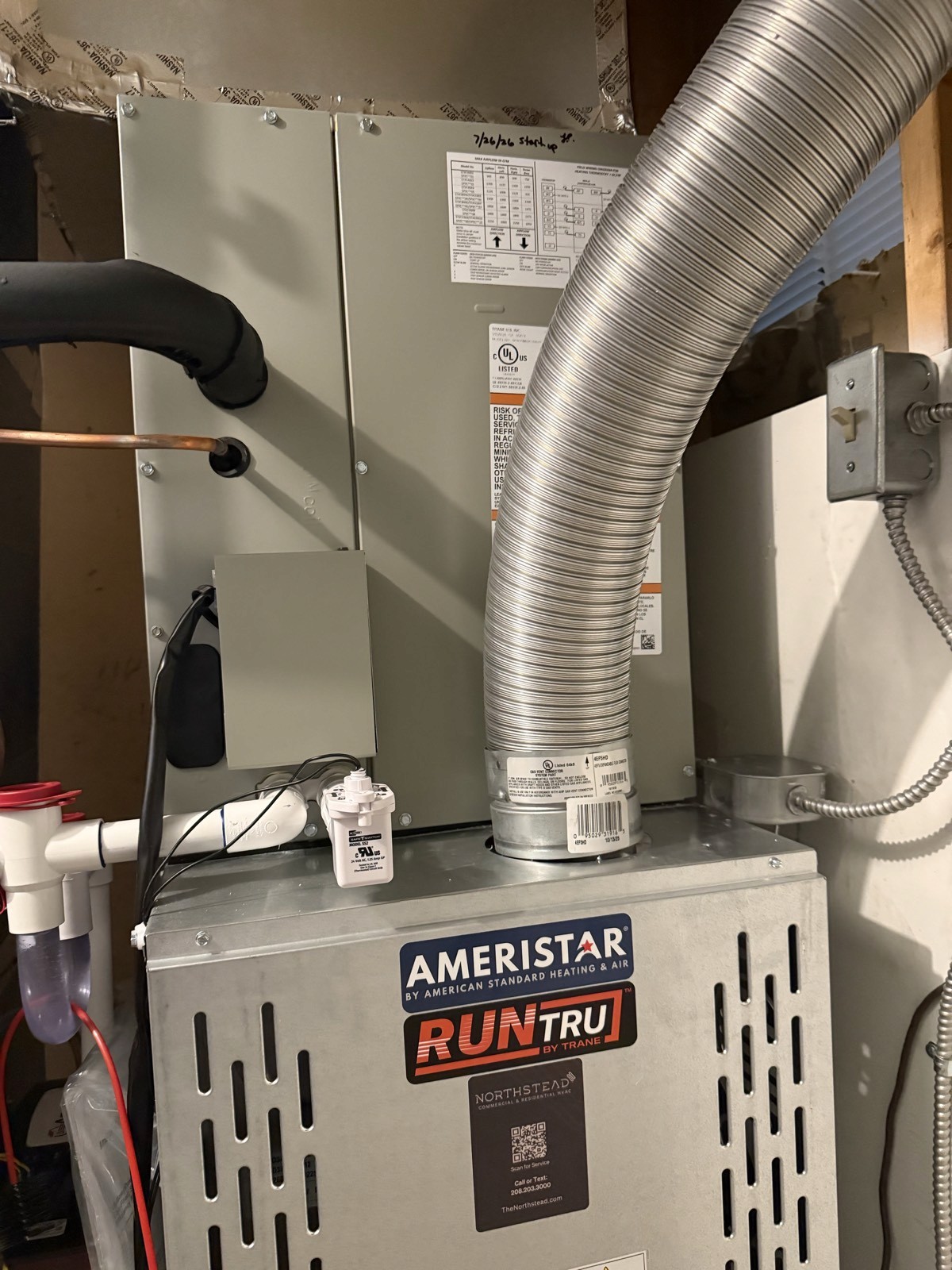 Top of a new gas furnace with flue connector, float switch, and condensate drain lines.