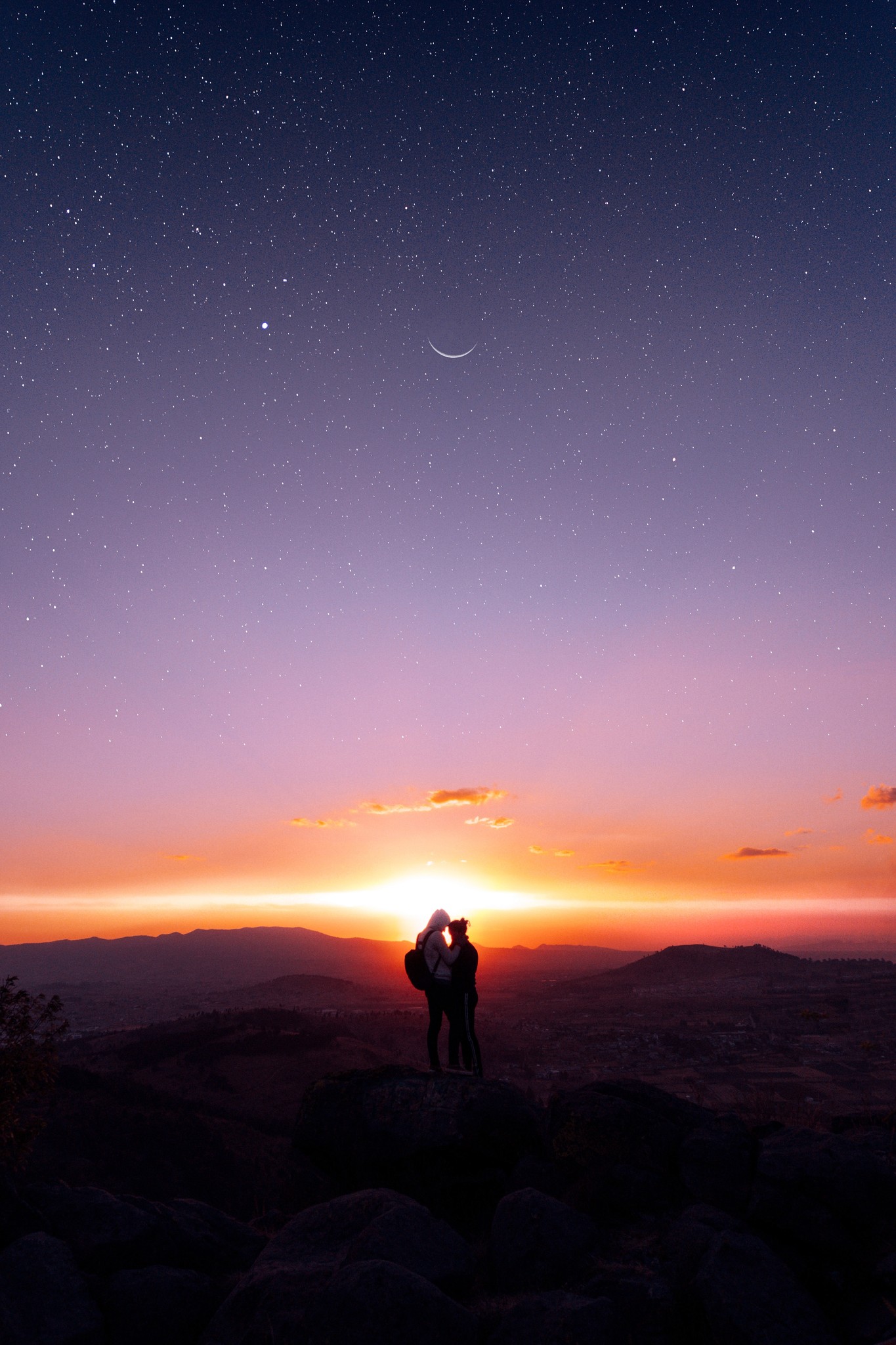 Two people holding each other looking at the sunset from the top of a mountain