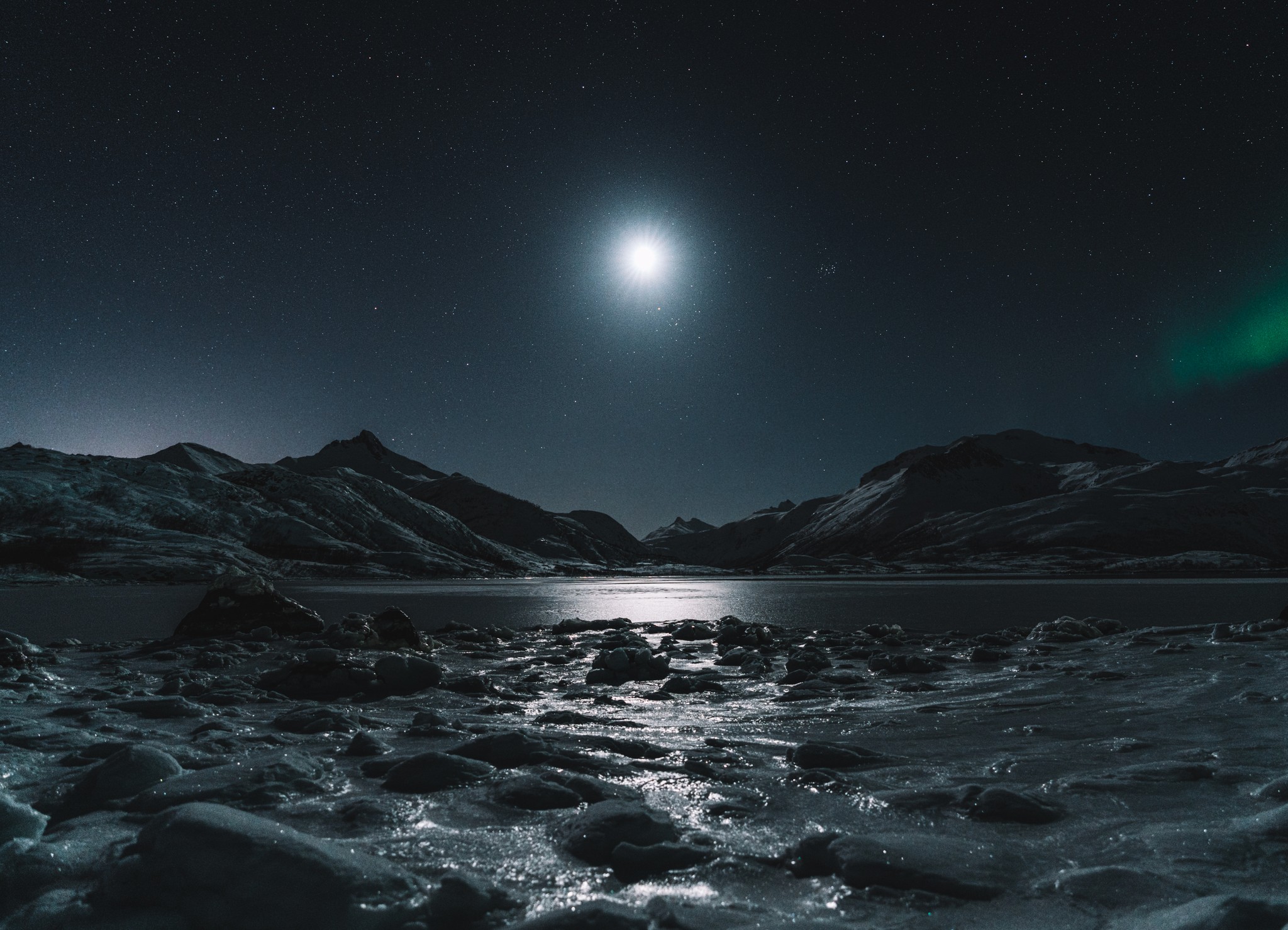 The glow of the moon over an icy lake with mountains in the background