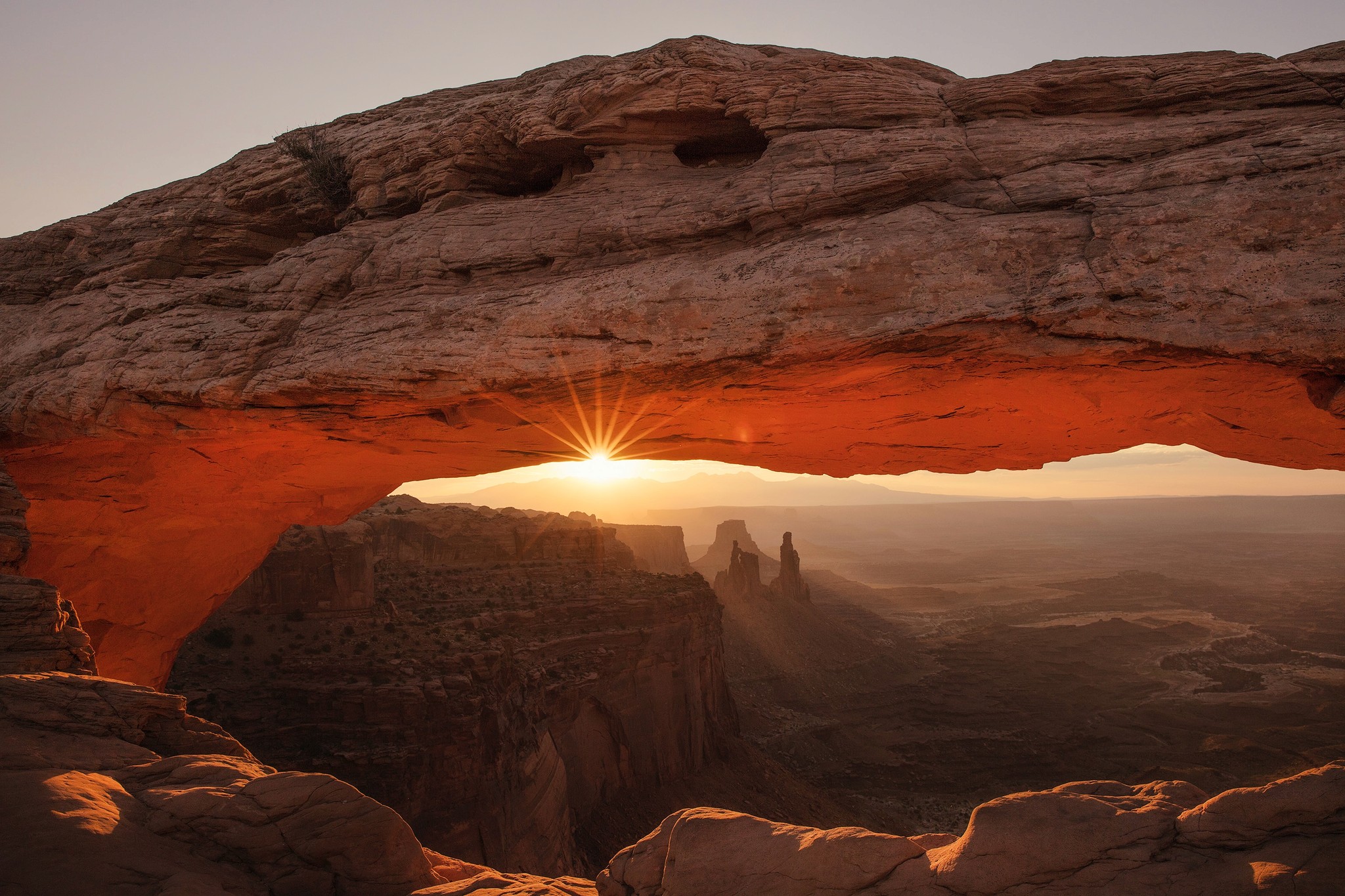 The sun peaking through a rocky arch formation at sunset