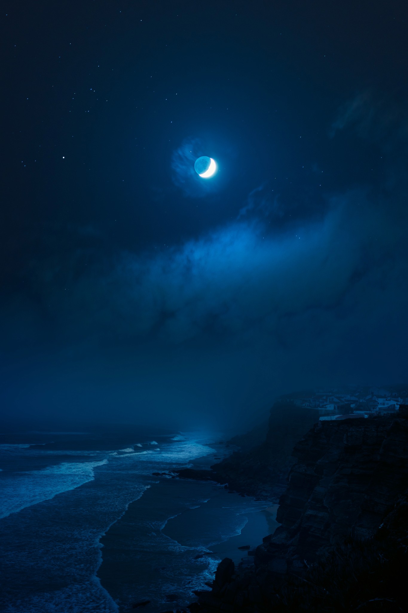 Cliffs overlooking a sandy beach and waves with a crescent moon in the sky