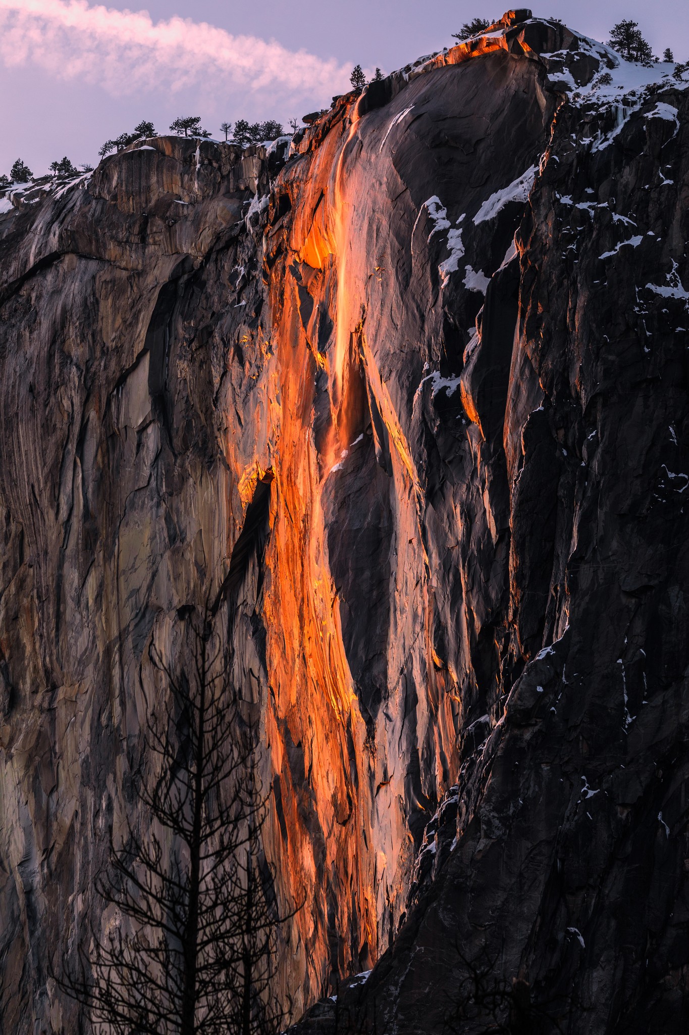 A rocky cliff with a waterfall illuminated by the orange glow of sunlight