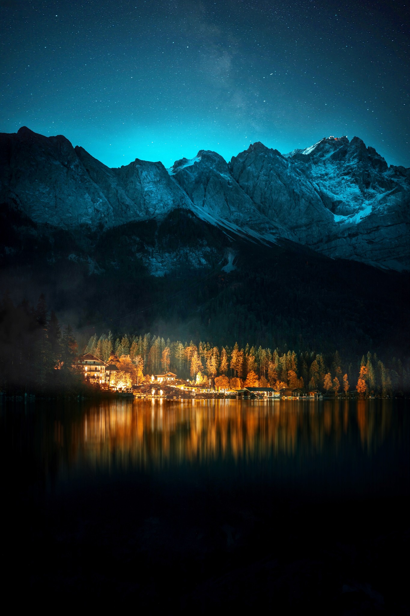 Houses on the edge of a lake with a warm glow and mountains in the background