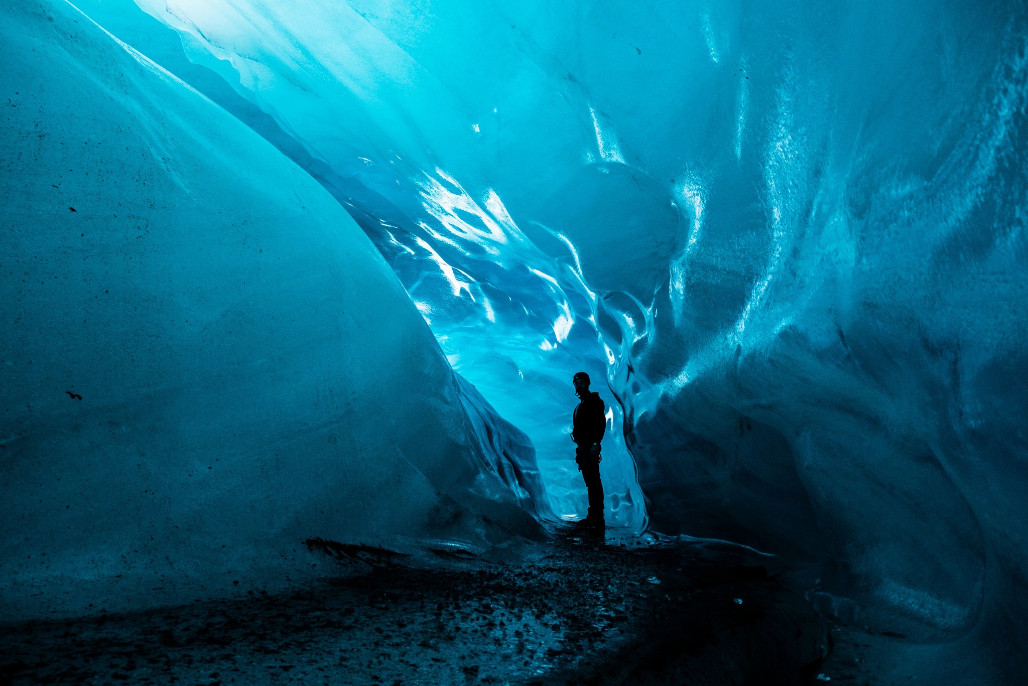 A person standing inside an icy blue cave near an opening