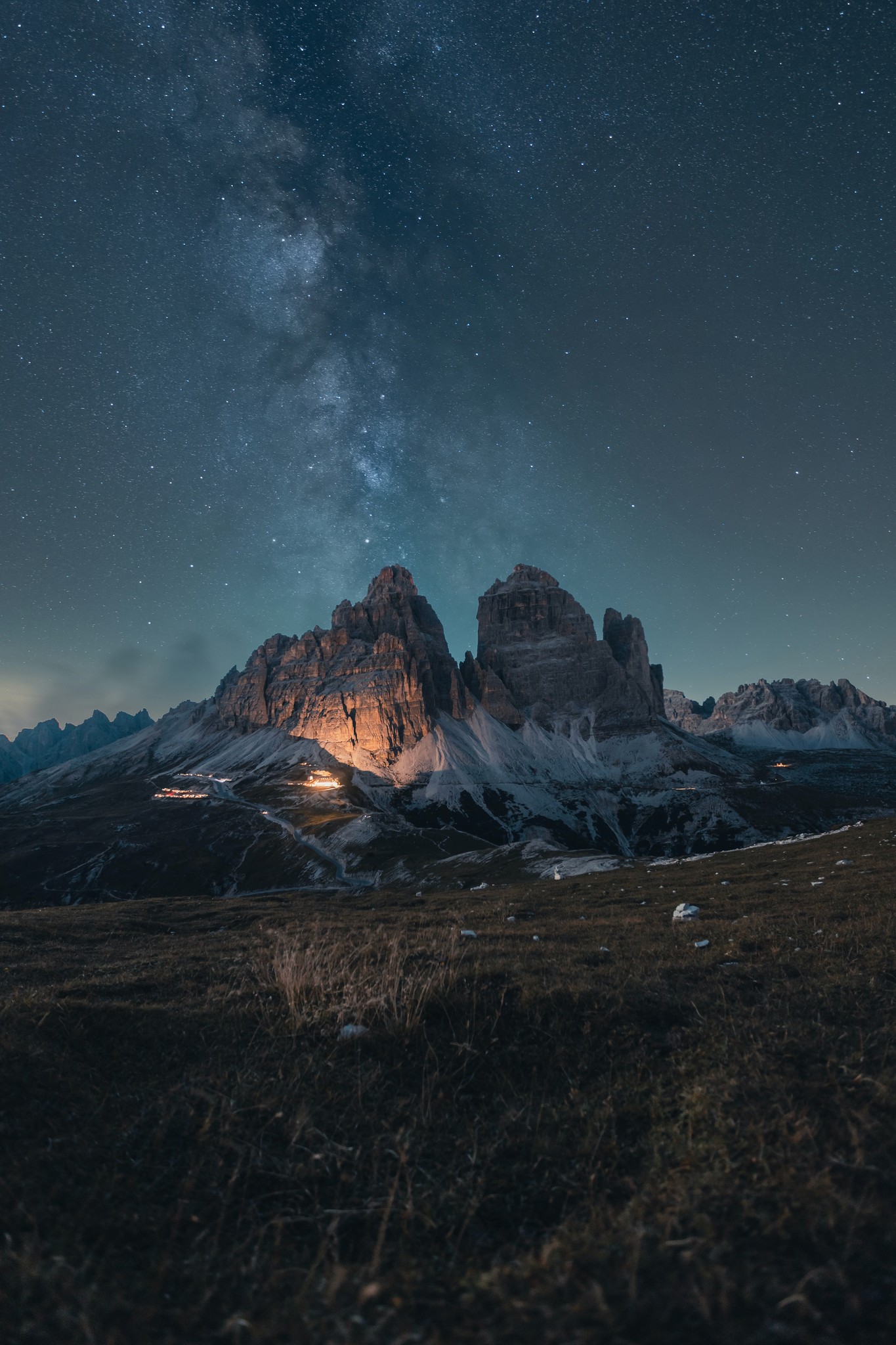 A mountain at the end of a grassy field illuminated by a light on a starry night