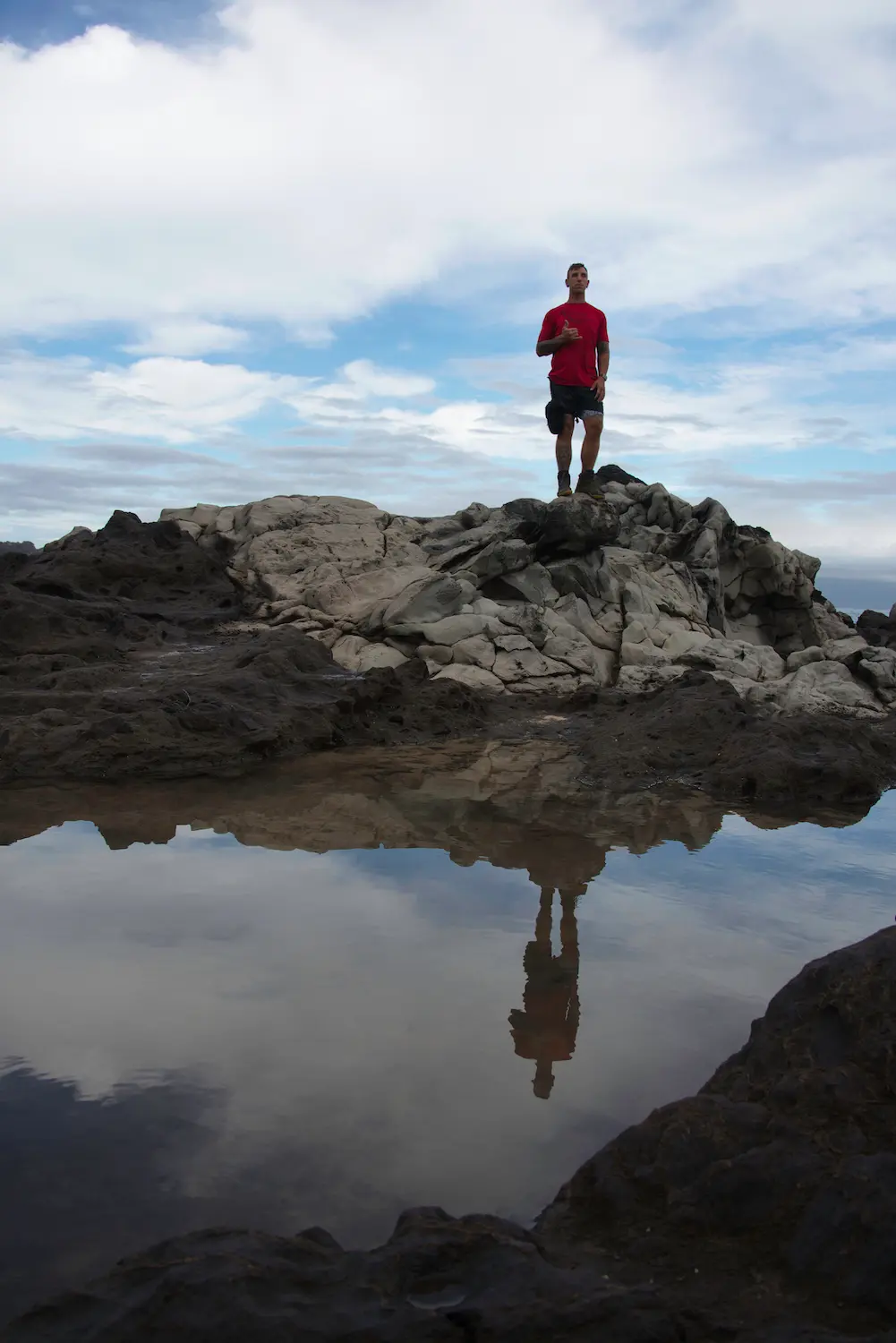 person standing on rock by the beach in maui with his reflection in the foreground on the water taken by professional travelling photograher