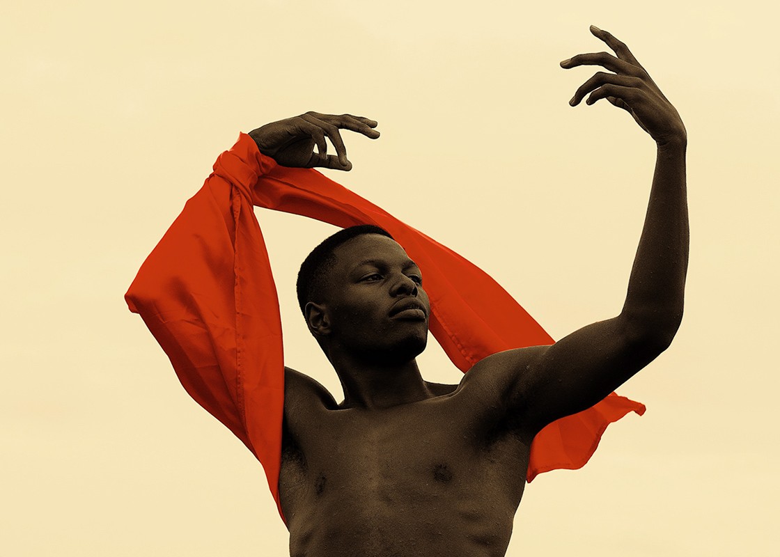 A medium shot of an African man gracefully holds up his arms, in an artistic fashion