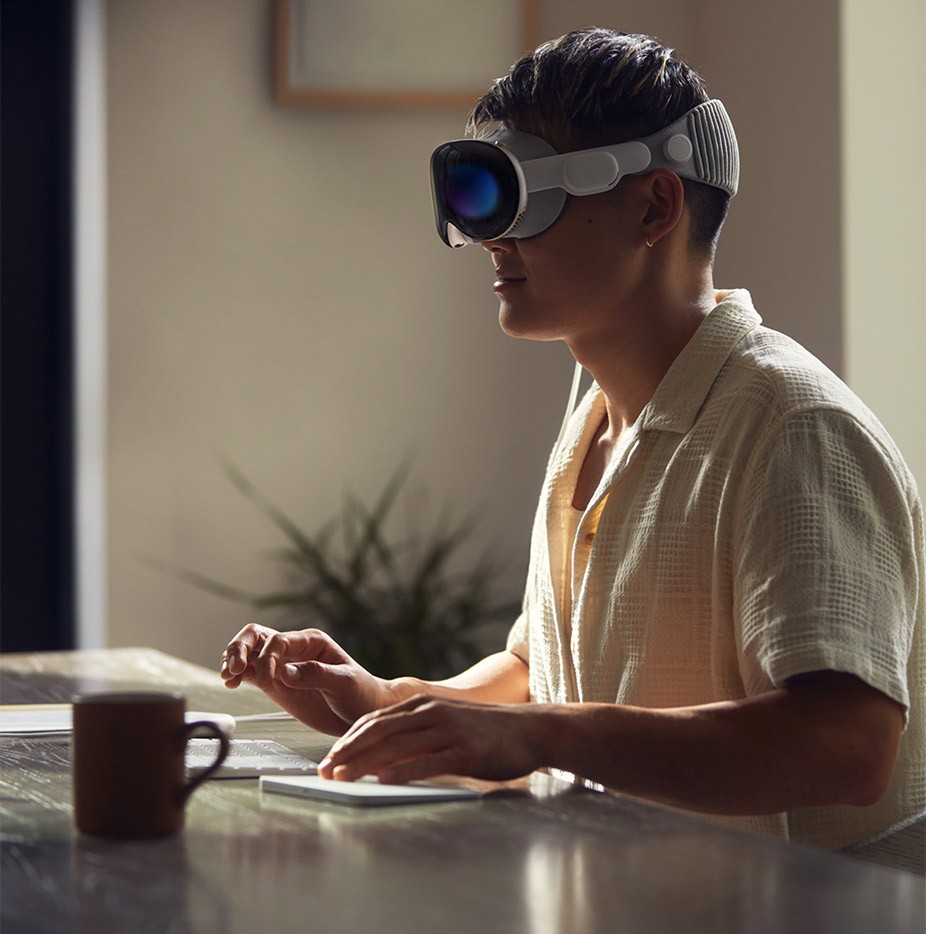 A medium shot of an Asian male using the Apple Vision Pro device at their workspace