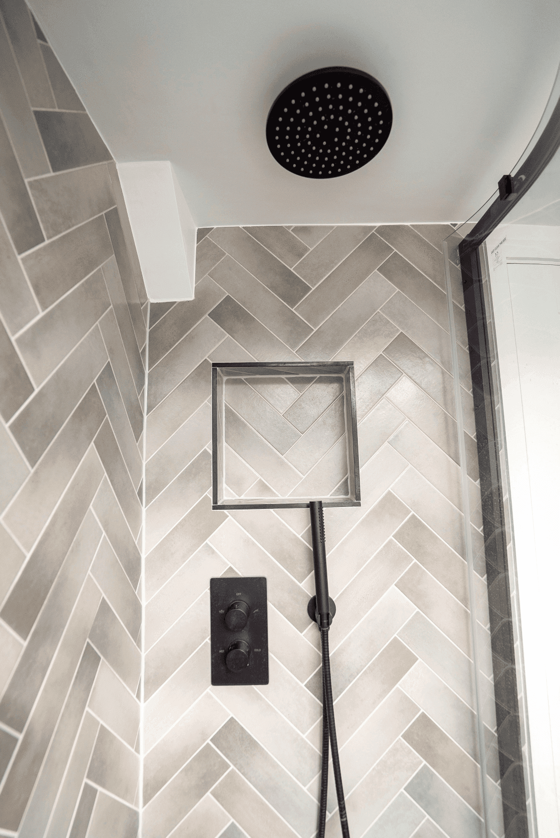 A herringbone tiled shower with a shower head in South West London.	