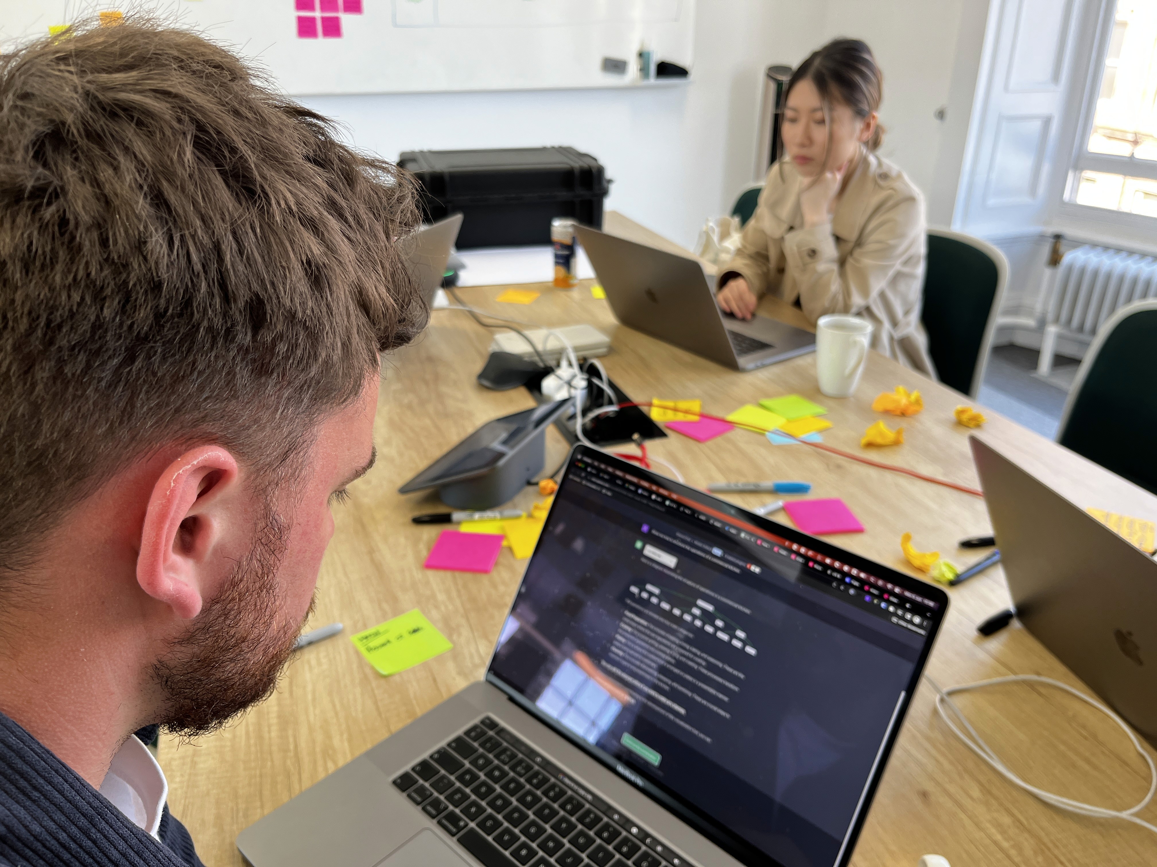 Two people working on the laptop at a table with post-it notes 