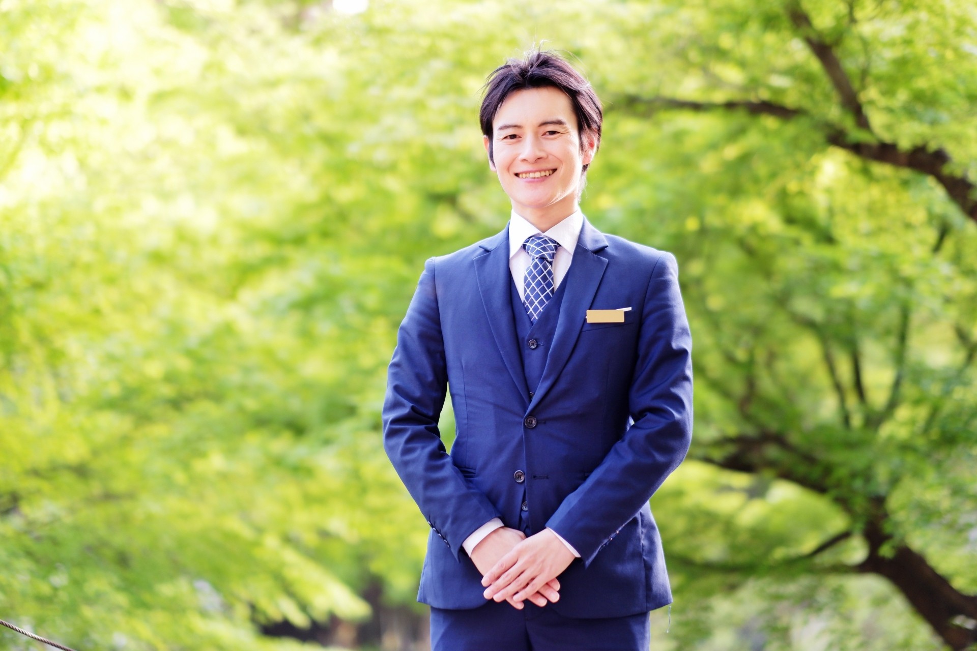 新緑の中でビジネスマンが立ってこちらを見ている