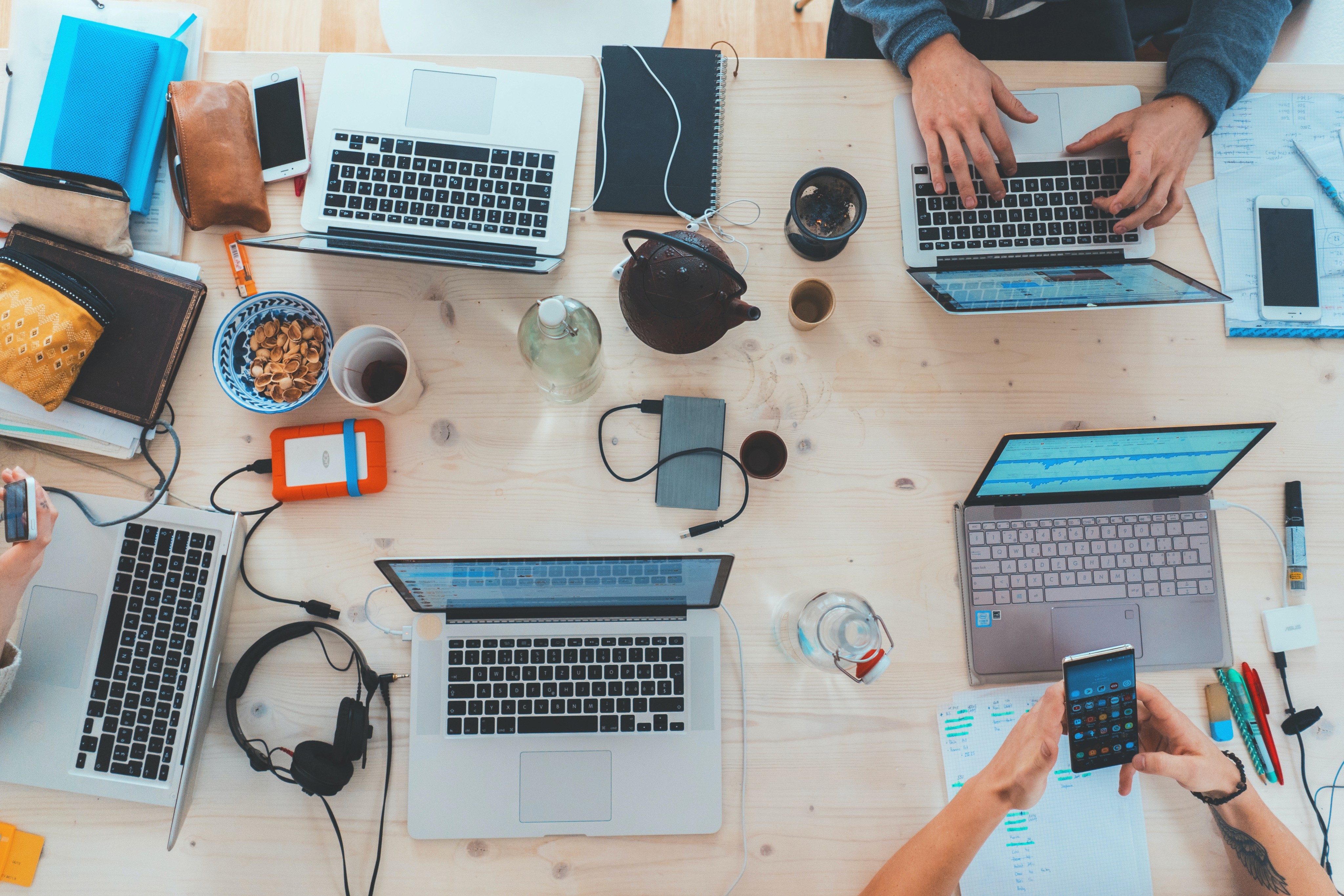 aerial picture of multiple people with their laptops on top of a light wood desk