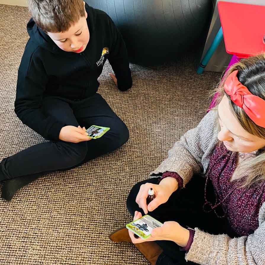 A facilitator and a child are sat on a carpet in the classroom. They are playing a game of Top Trumps